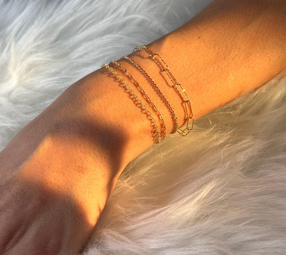 Stack of gold and silver permanent chain bracelets on a wrist